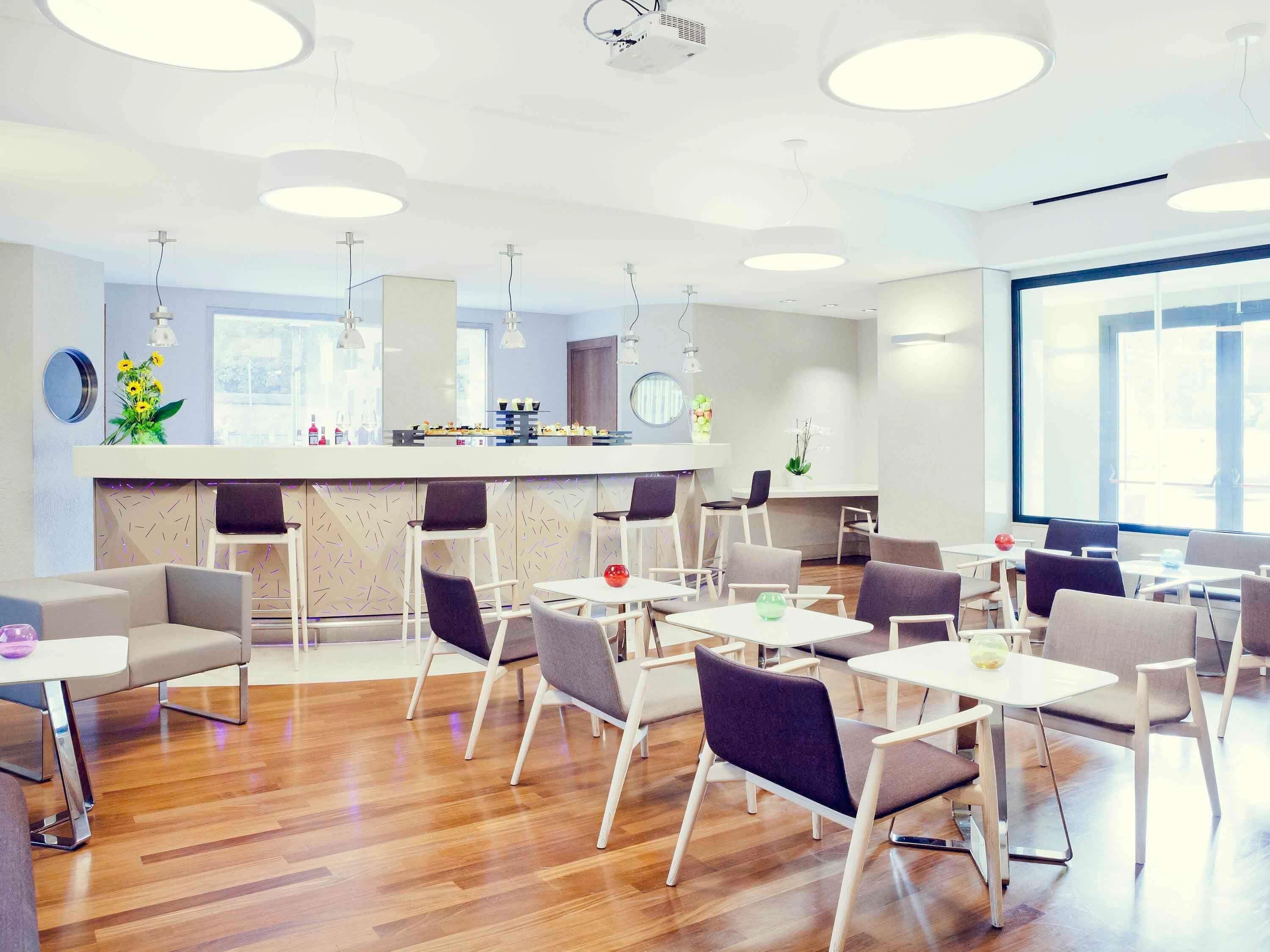 A modern interior with a bar area, multiple seating arrangements, and a large window providing natural light.