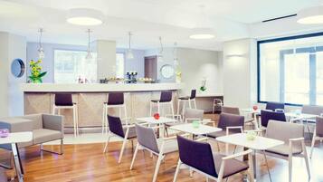 A modern interior with a bar area, multiple seating arrangements, and a large window providing natural light.