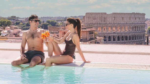 Una pareja sentada junto a una piscina con vistas al Coliseo de Roma.