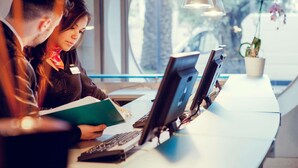 Un espacio de oficina moderno con dos personas en sus escritorios, una sosteniendo un documento.