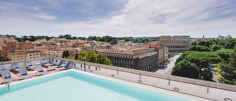 A rooftop pool with lounge chairs, a clear view of the cityscape, and the Colosseum in the background.