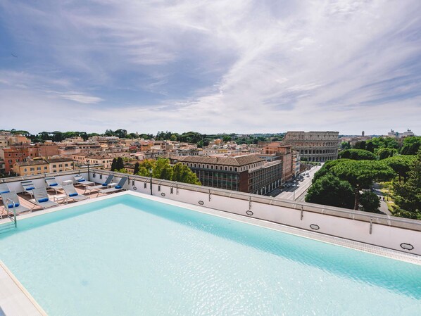 A rooftop pool with lounge chairs, a clear view of the cityscape, and the Colosseum in the background.
