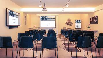 A conference room with rows of chairs, a projector screen, and presentation slides on the wall.