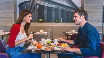 Dos personas cenando en una mesa con un mural de un paisaje urbano al fondo.