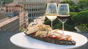 Un plato con pan, queso y embutidos, dos copas de vino y vistas del Coliseo en Roma.