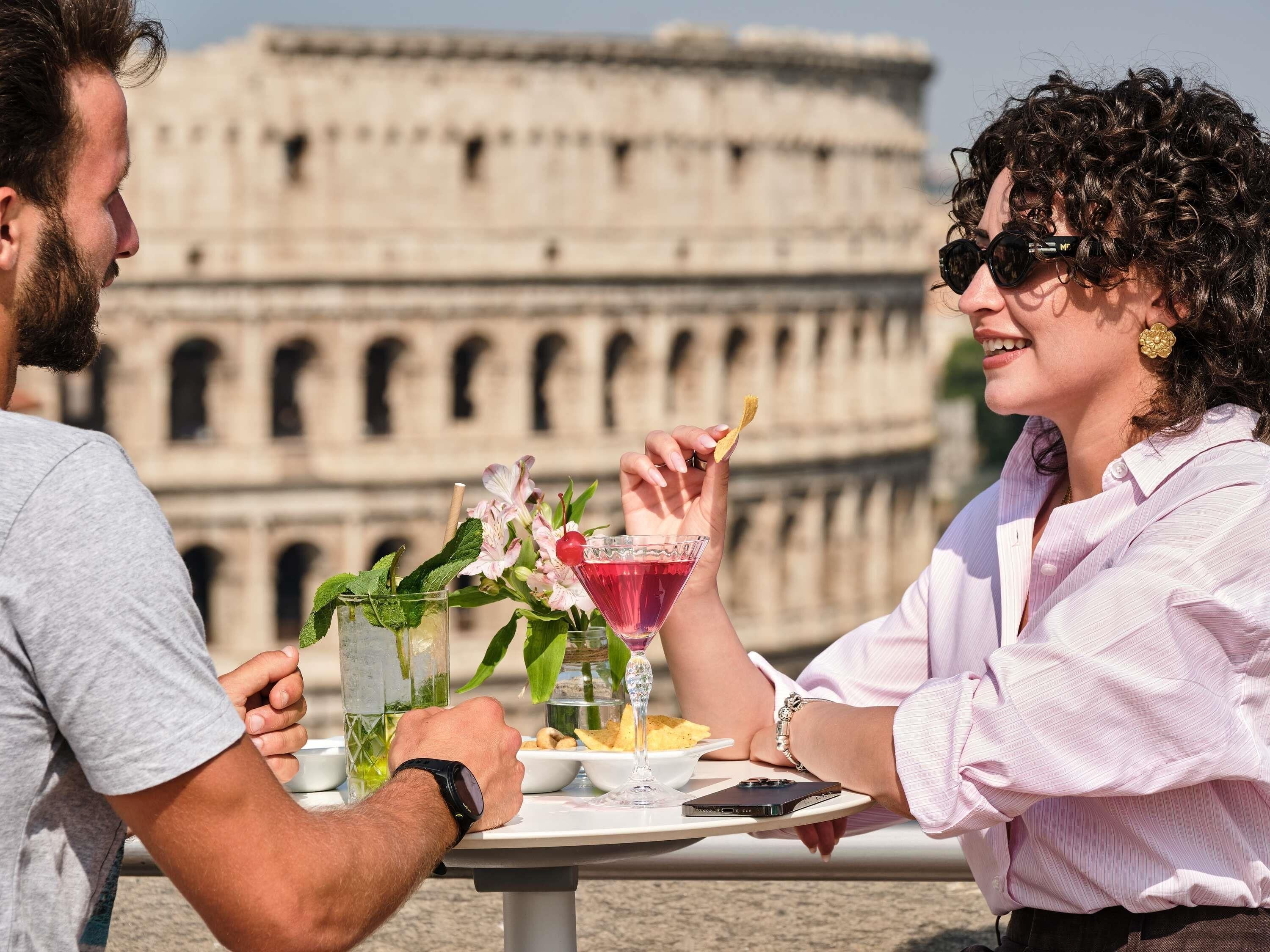 Una coppia cena all'aperto con vista sul Colosseo sullo sfondo.