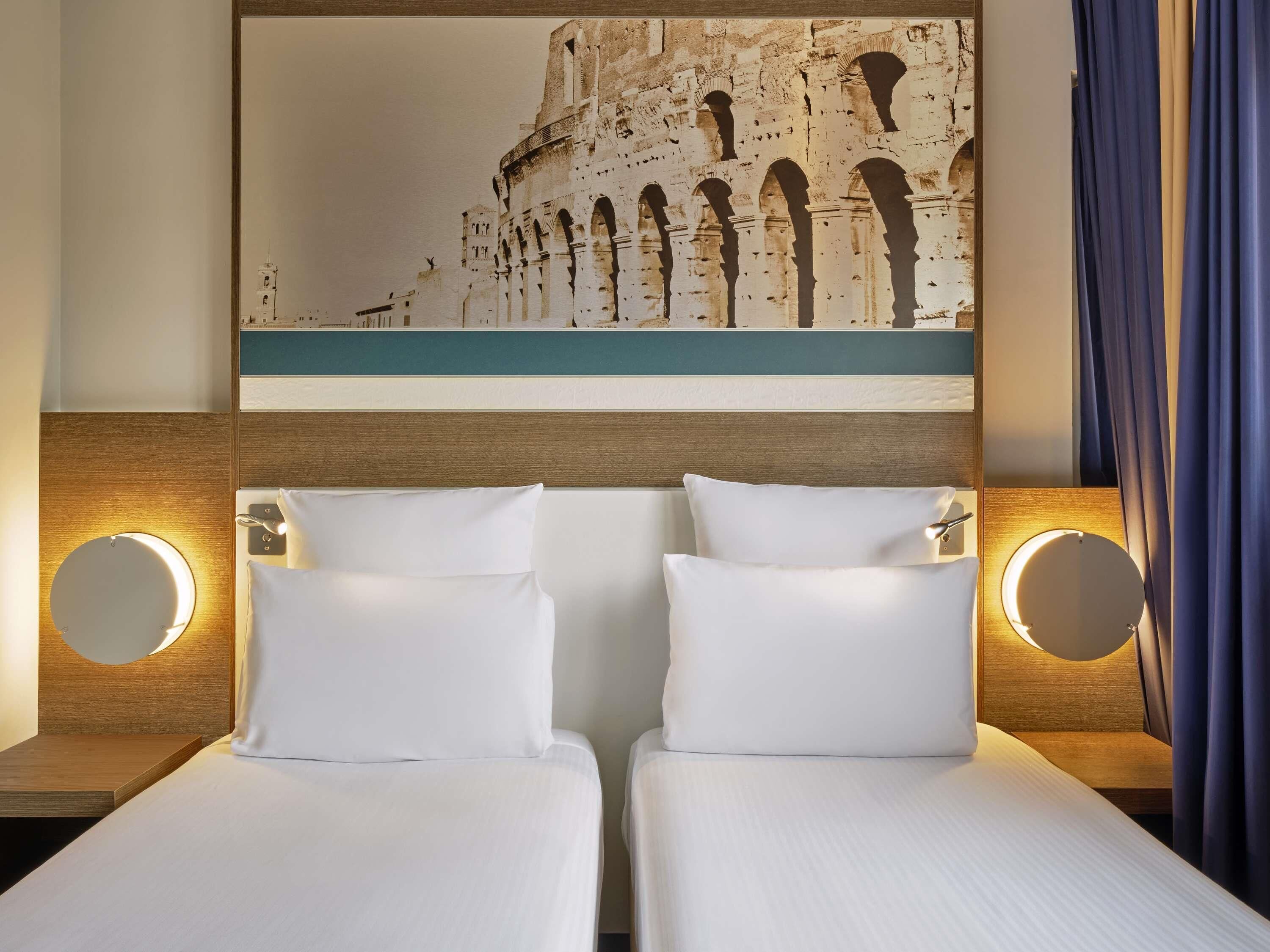 A hotel room with two beds, a large painting of an ancient structure, and two bedside lamps.