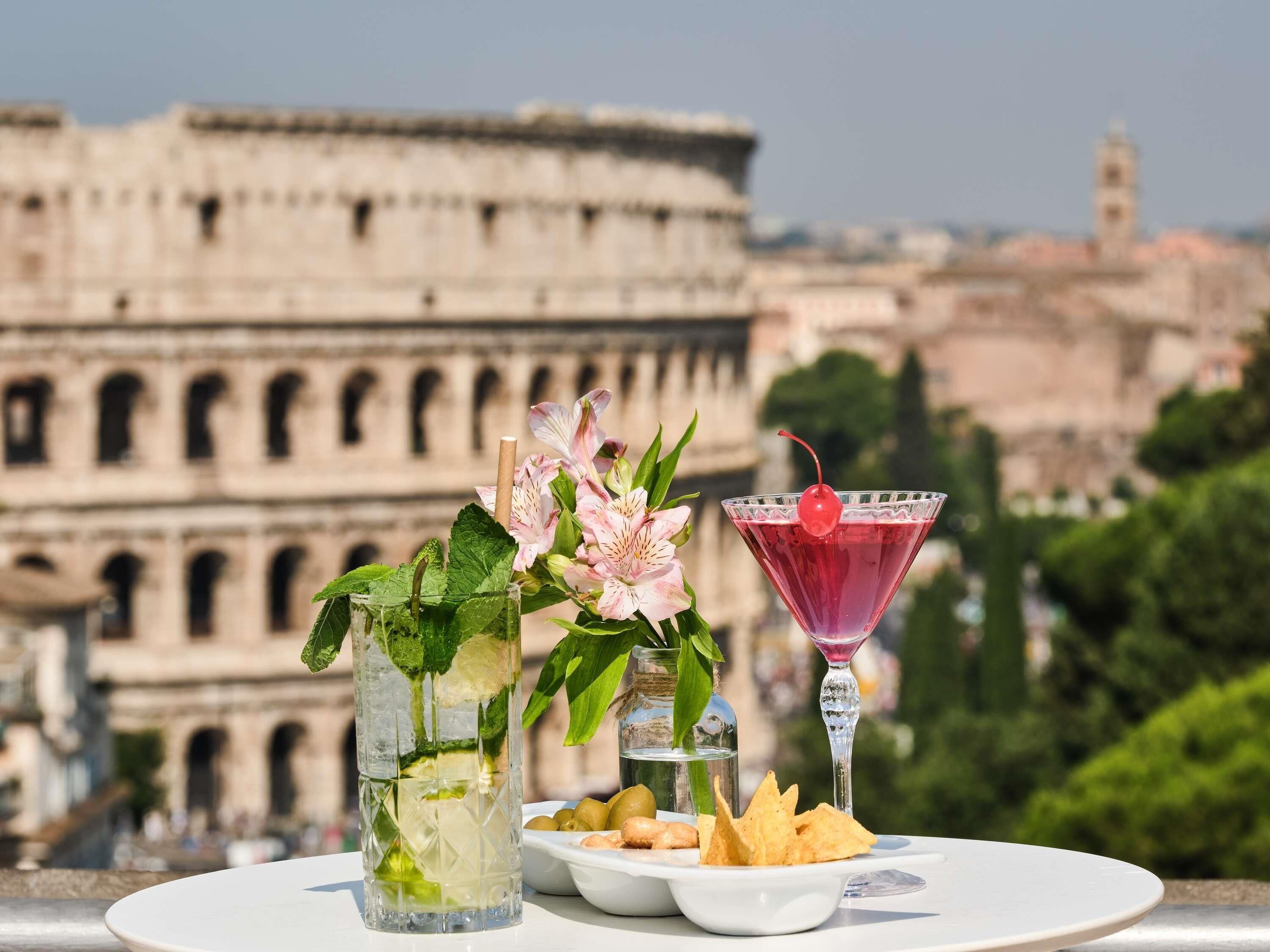 A table with a drink, flowers, and snacks against a backdrop of the Colosseum.