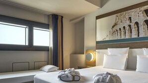 Habitación de hotel con una cama grande, una mesita de noche, una lámpara, una ventana con cortinas y un cuadro del Coliseo.
