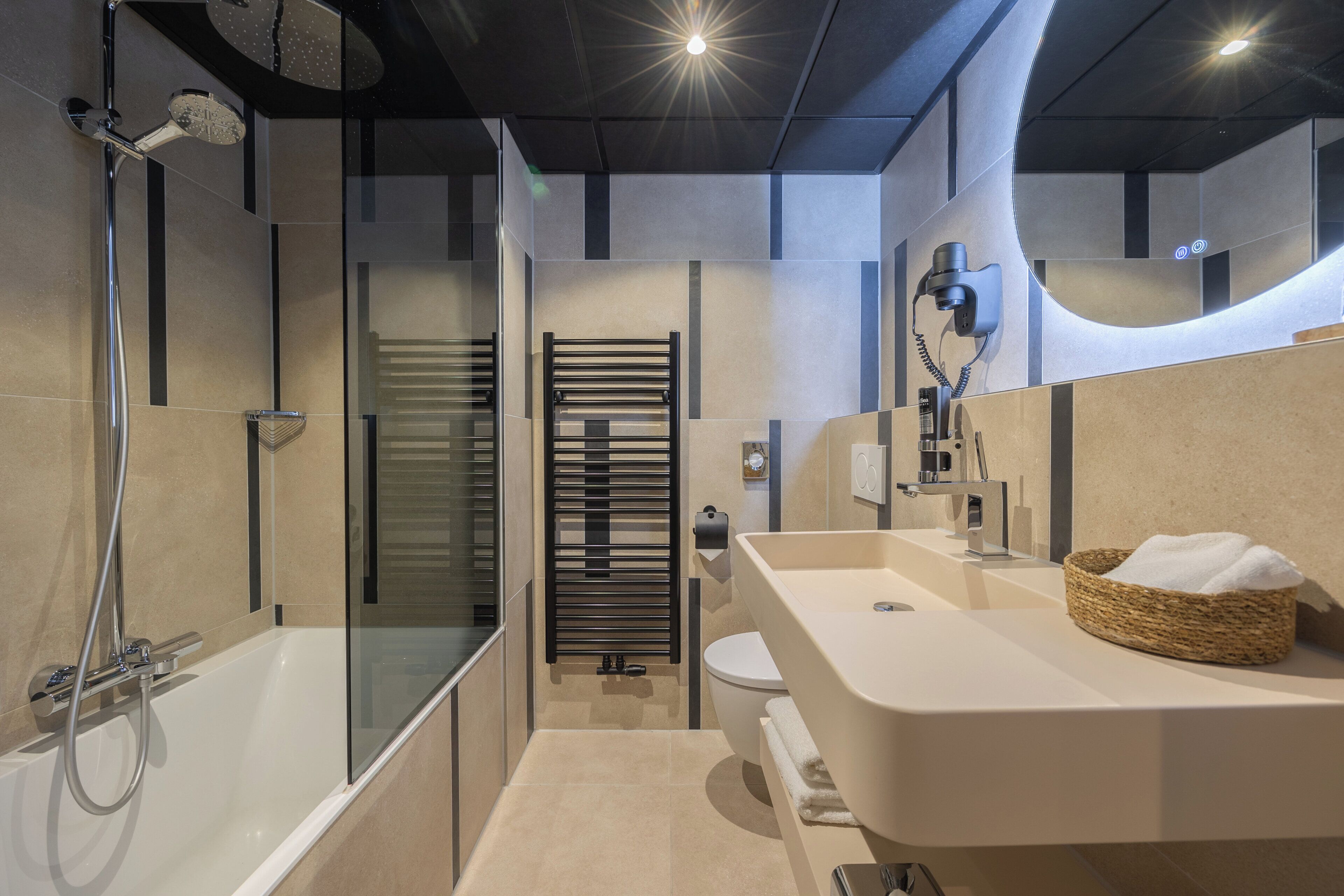 Un baño moderno con bañera, inodoro y tocador con una cesta de toallas.