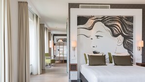 Una habitación de hotel con una cama grande, un mural en la pared y un pasillo con un escritorio y una silla.