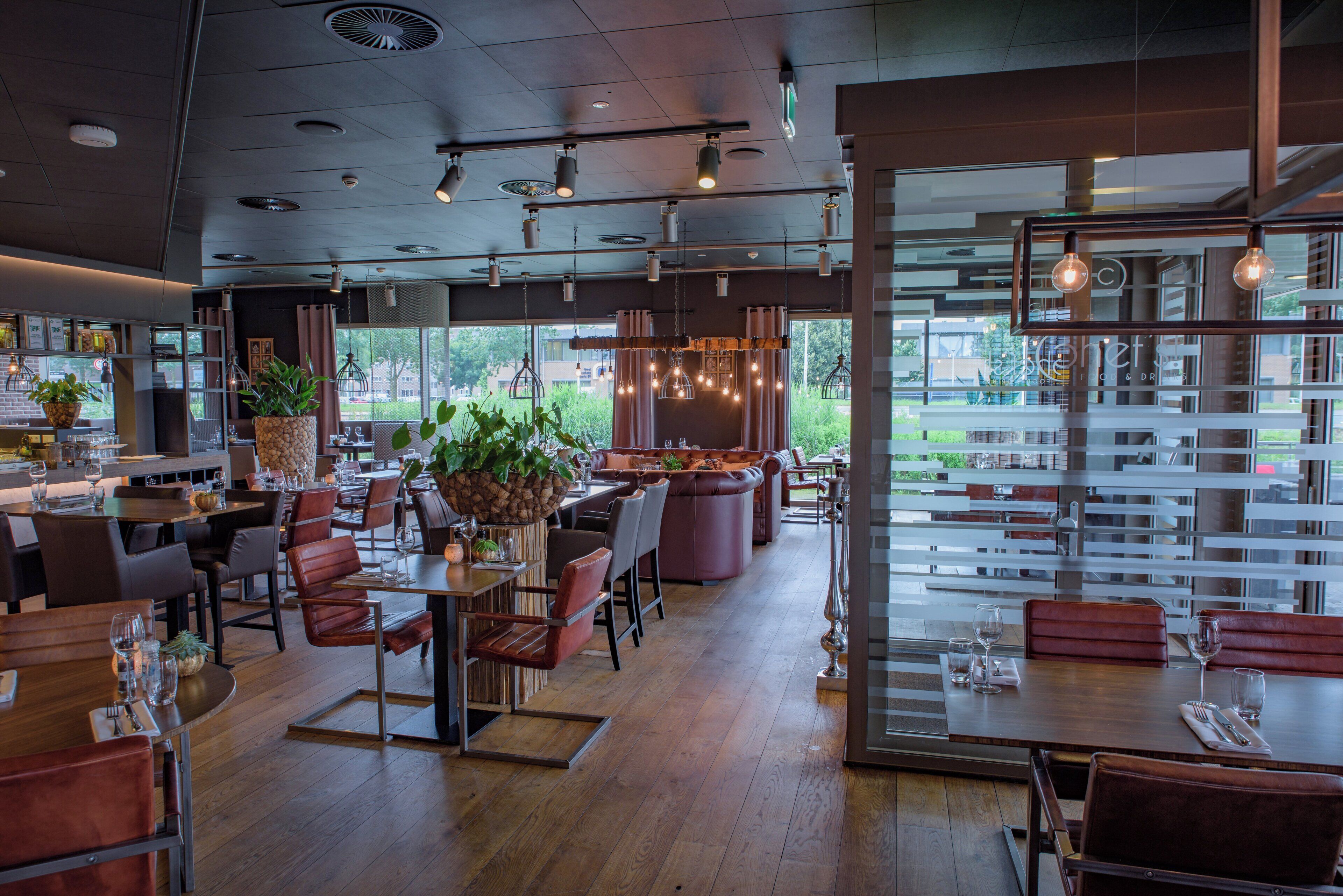 A modern restaurant interior with wooden tables, leather booths, and hanging pendant lights.