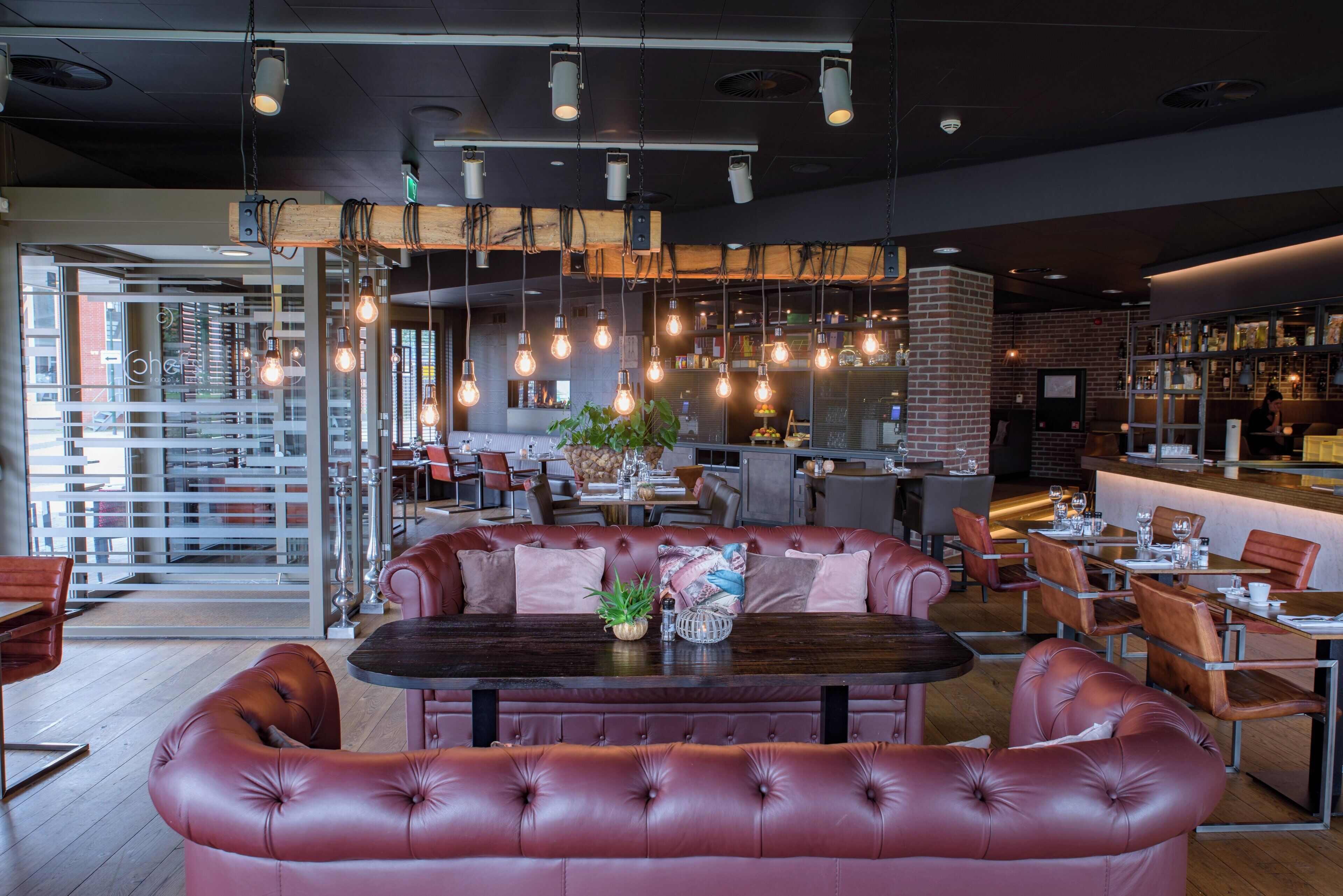 Un interior de restaurante moderno con una zona central de asientos que incluye una mesa de madera oscura y cabinas de cuero rojo.