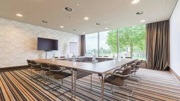 A conference room with a long table, multiple chairs, a flat-screen TV, and large windows with curtains.
