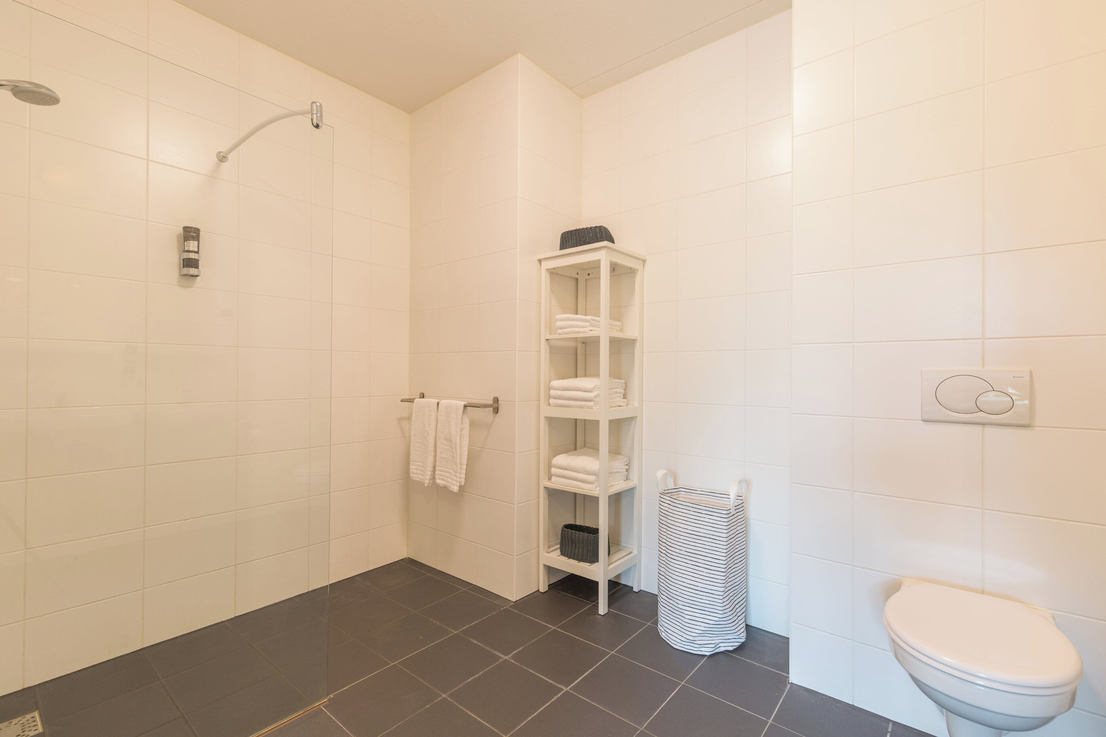 A modern bathroom with white tiles, a shower, a toilet, and a towel rack.