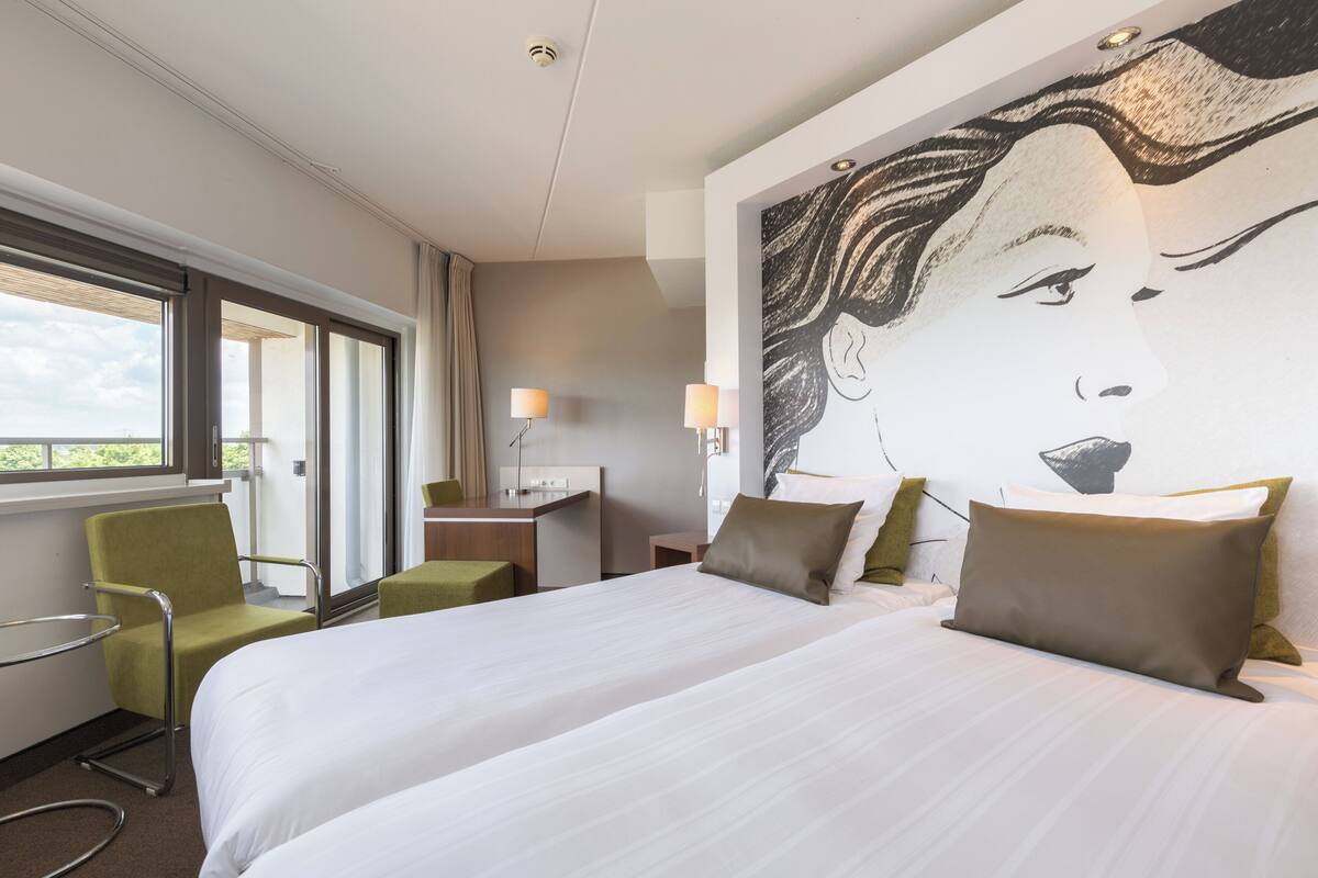 A hotel room with a large bed, a desk, a chair, and a window with curtains.