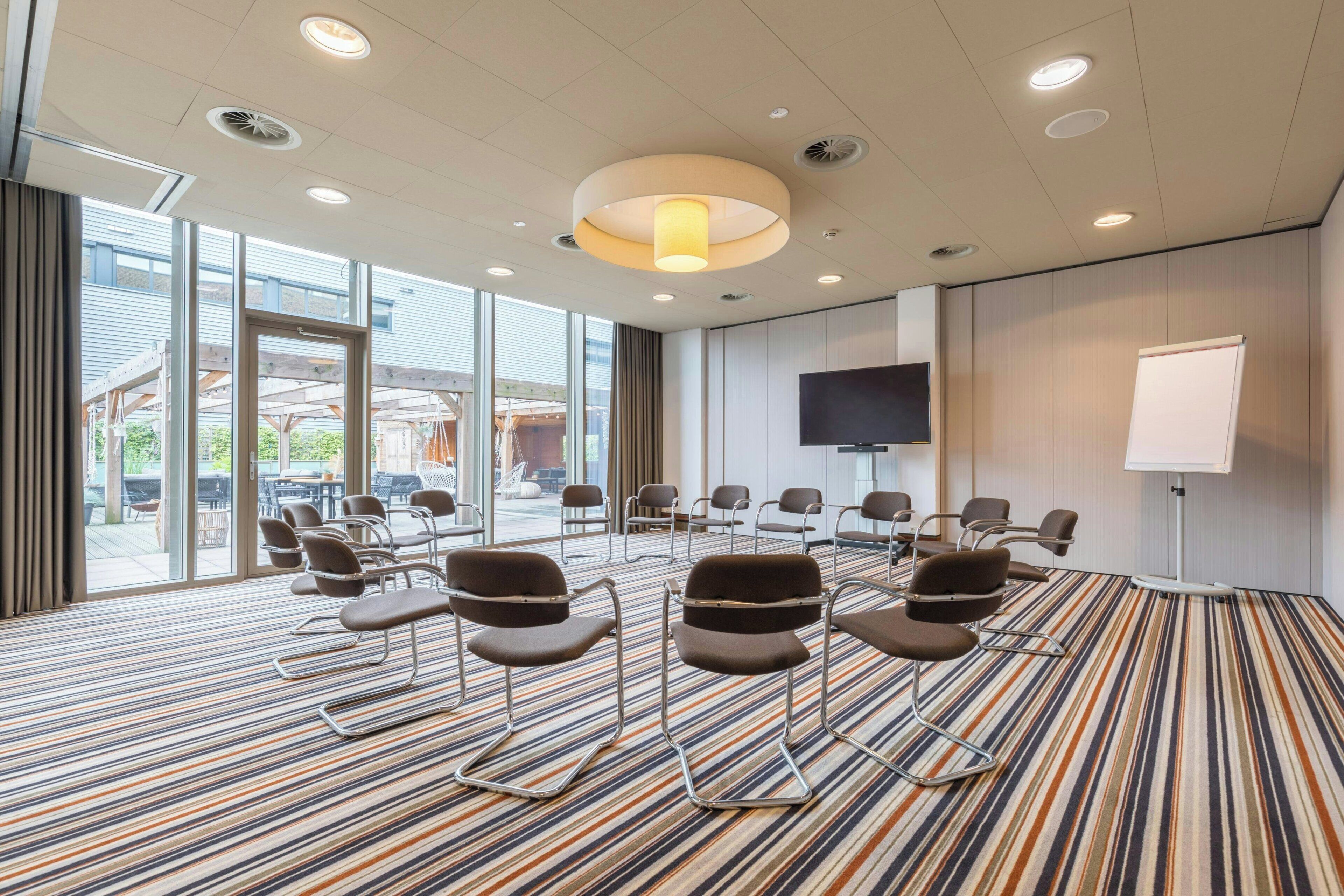 A conference room with a striped carpet, chairs arranged in a semi-circle, a large screen, and a whiteboard.