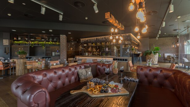 Un restaurante moderno con asientos de cuero, una mesa de madera con comida y una zona de bar al fondo.