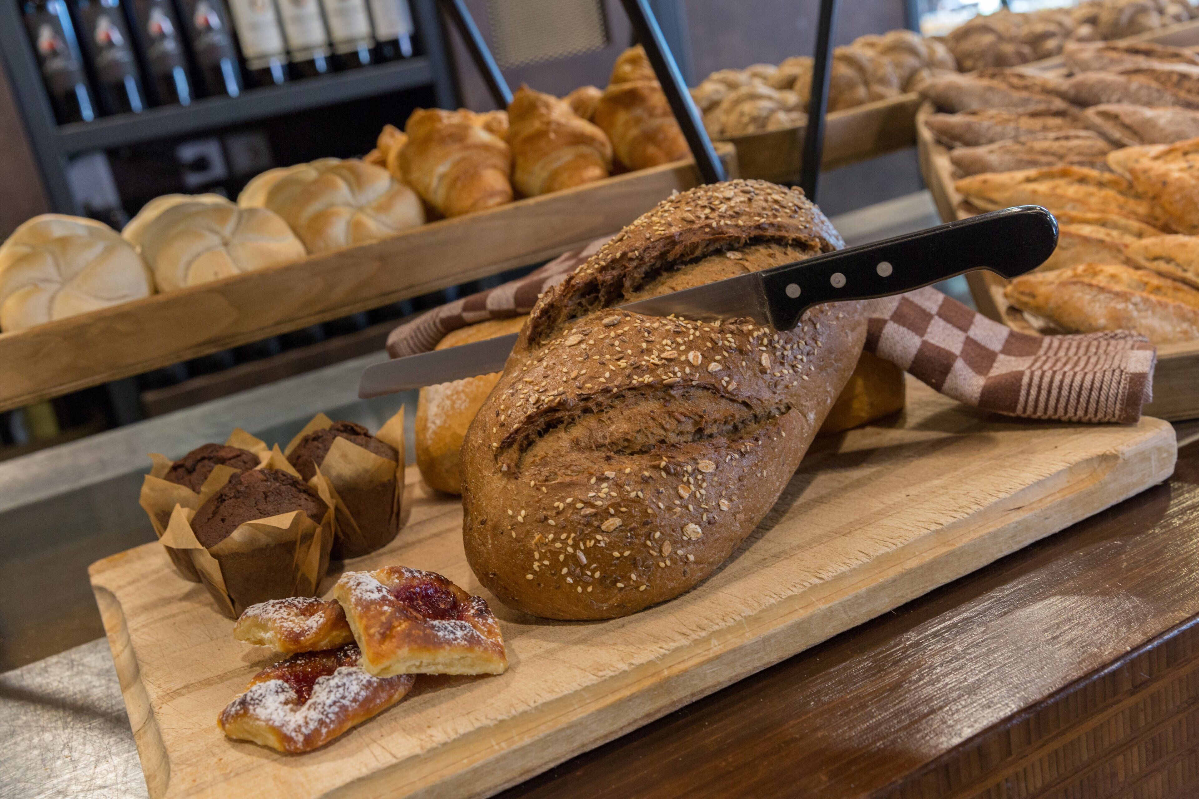 Diverse broden en gebak, waaronder een brood met zaden, gepresenteerd op een houten plank met een mes.