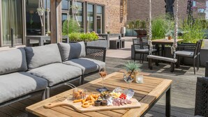 Un patio al aire libre con una mesa de madera dispuesta con comida, un sofá y asientos para exteriores.