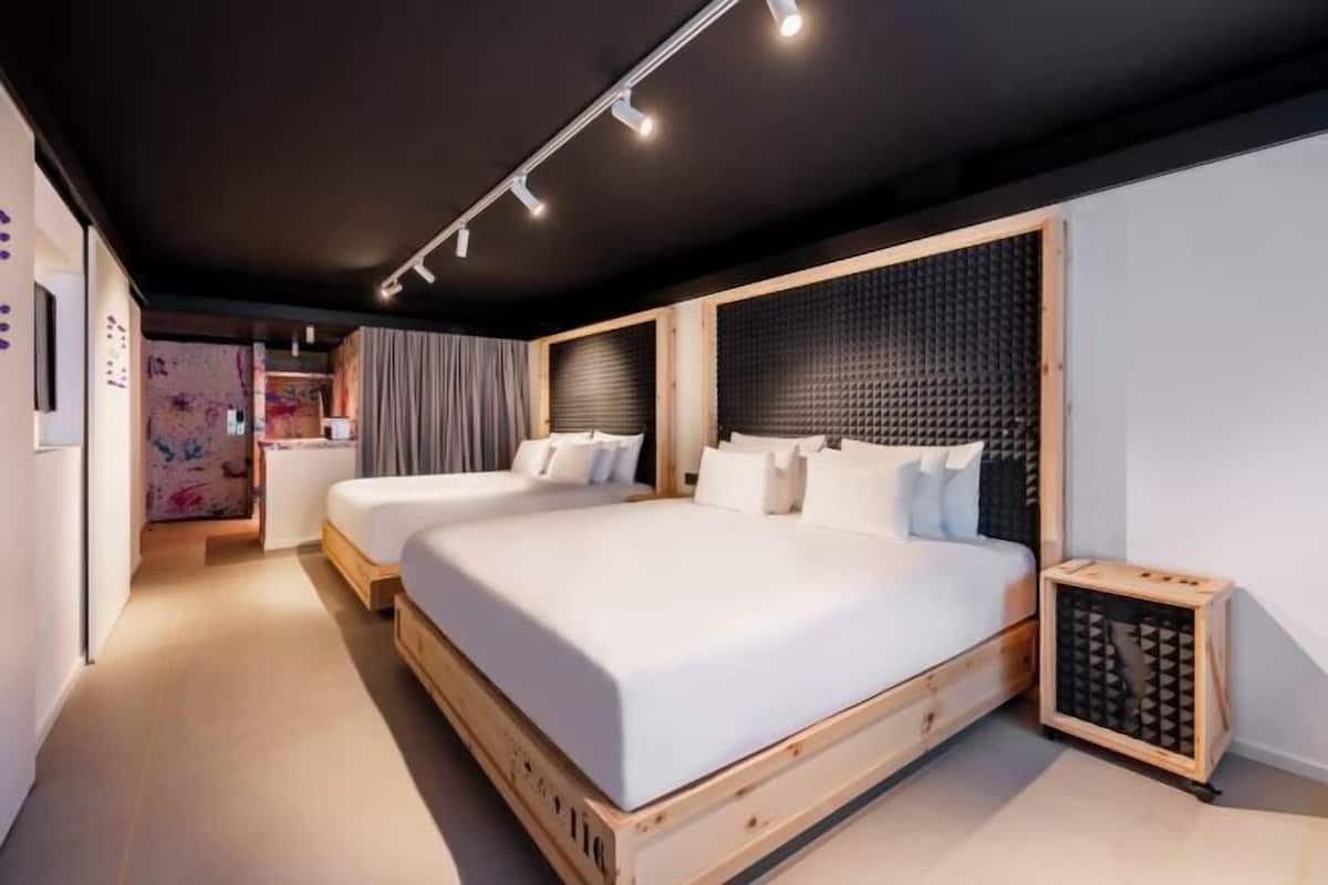 A modern bedroom with two beds, a wooden headboard, and a small bedside table.