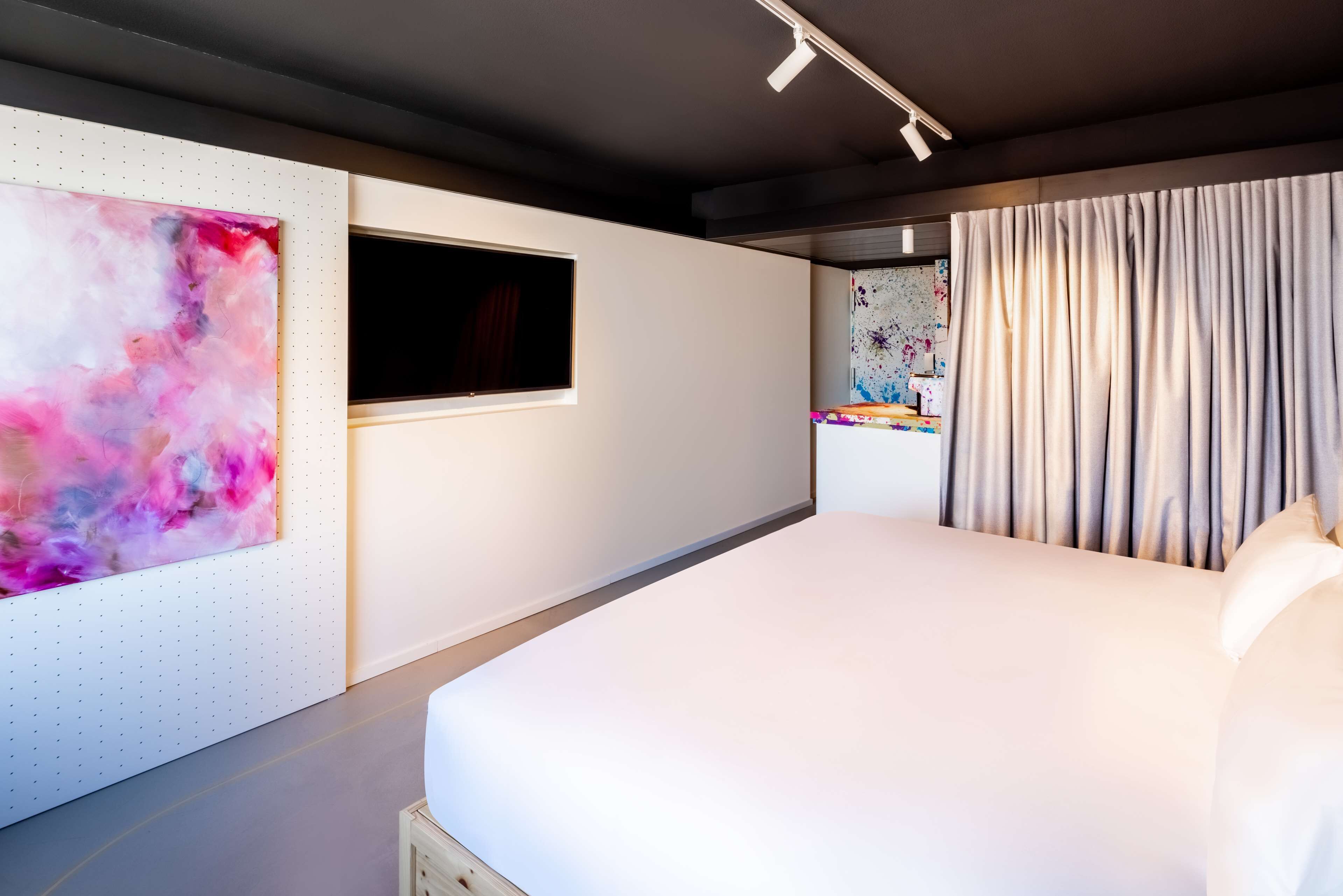 A modern hotel room with a large bed, a wall-mounted TV, and a colorful abstract painting.