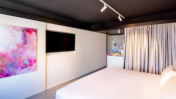 A modern hotel room with a large bed, a wall-mounted TV, and a colorful abstract painting.