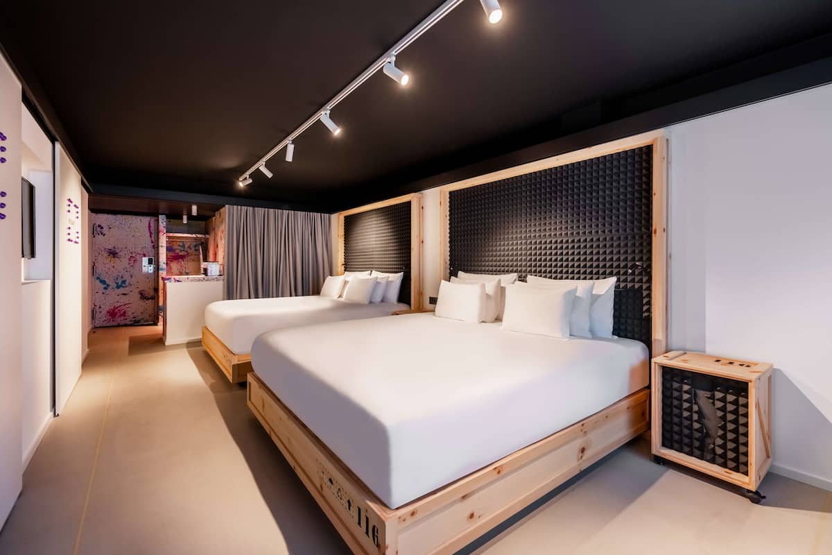 A modern bedroom with two beds, a wooden headboard, and a small wooden cabinet.