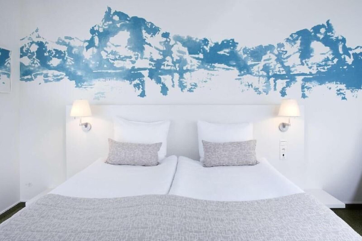 A double bed with two pillows, a headboard, and two wall-mounted lamps.