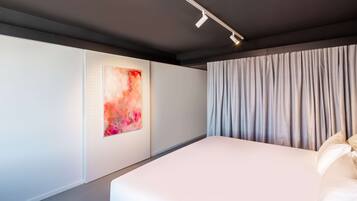 A modern bedroom with a large bed, a wall-mounted abstract painting, and a window with curtains.