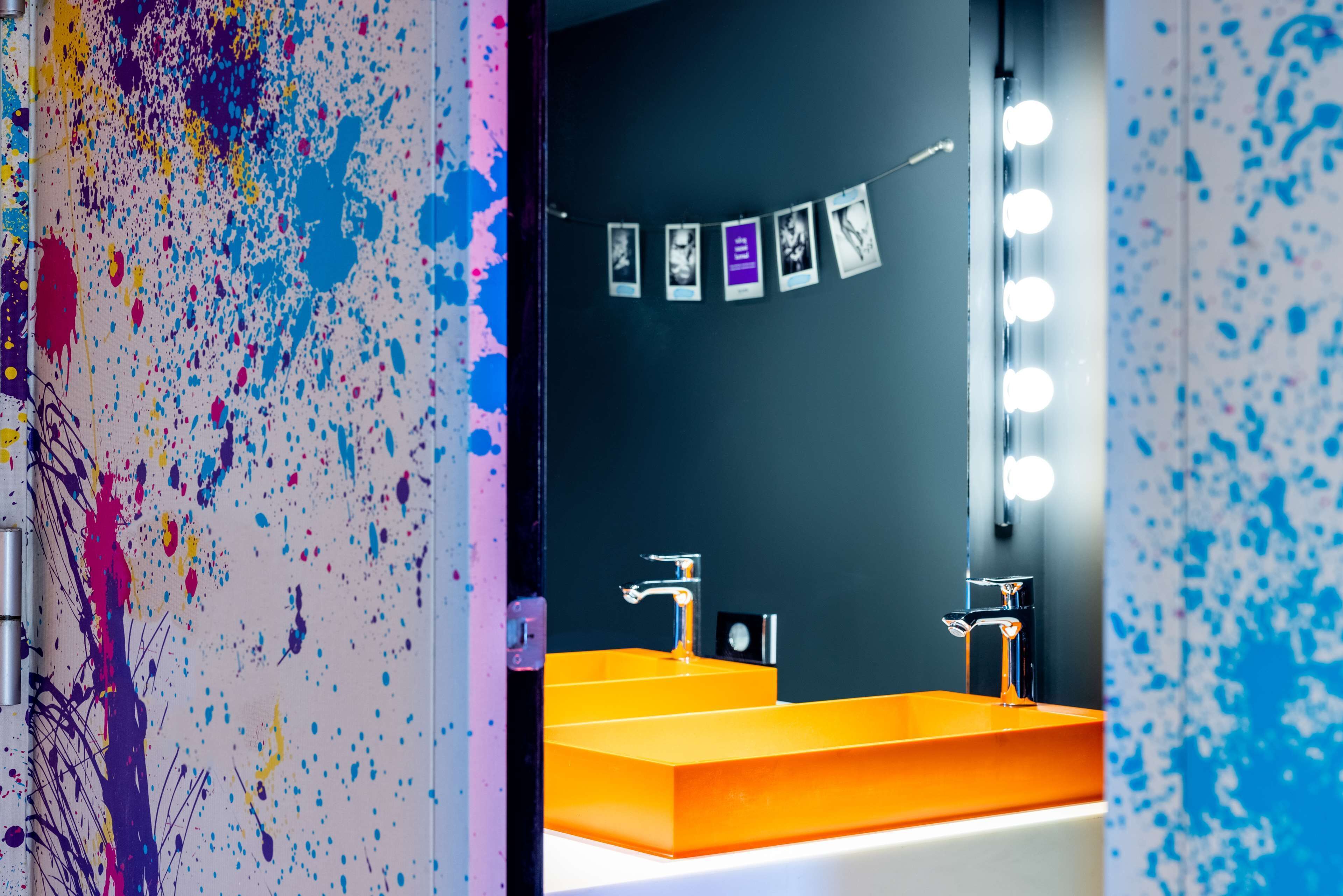 A bathroom with a modern design, featuring a large mirror, two sinks, and a wall with a series of photographs.