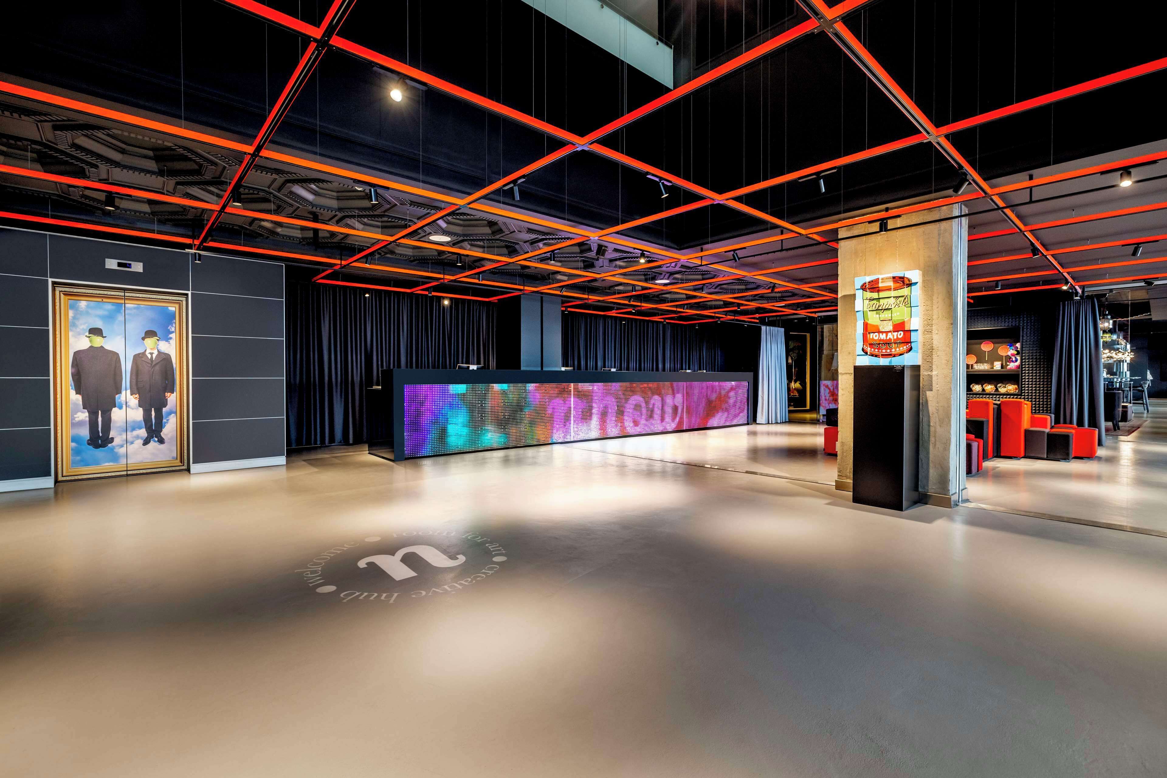 A modern lobby with a reception desk, a digital display, and a unique ceiling design.