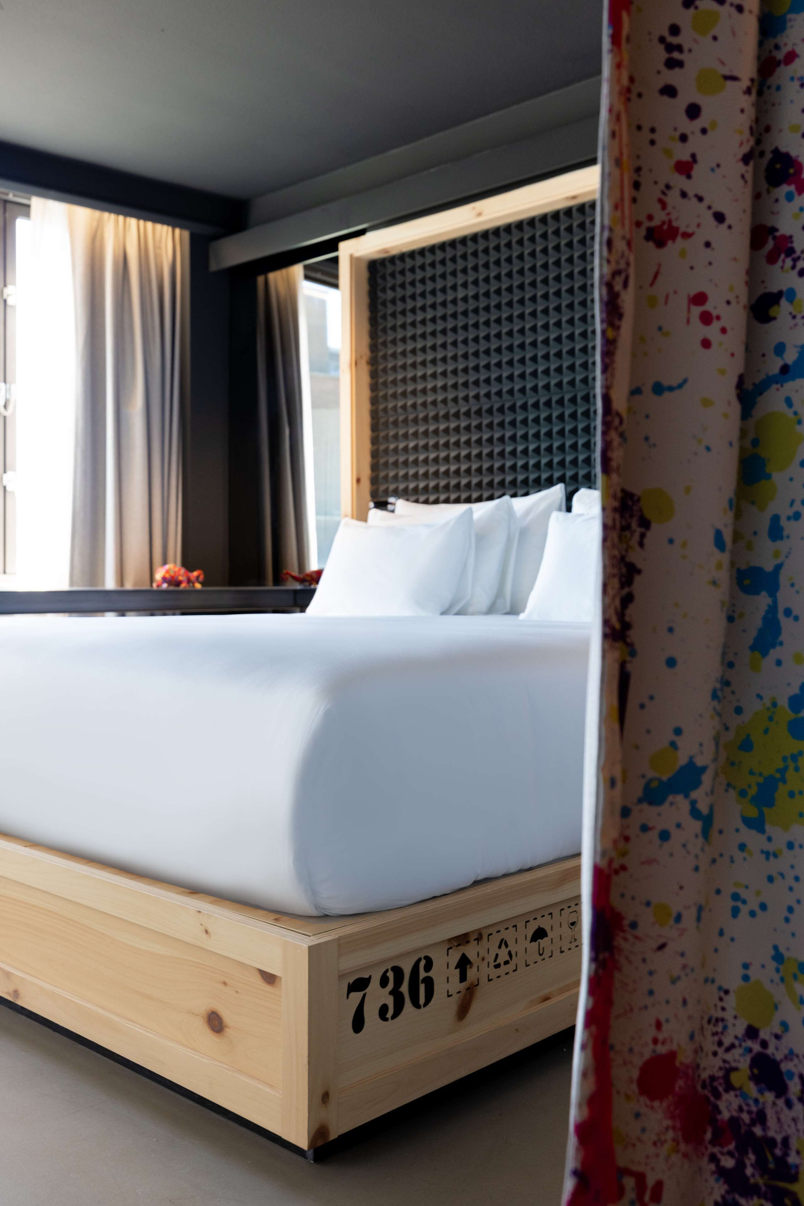 A wooden bed with a number "736" on the side, a headboard with a textured pattern, and a window with curtains.