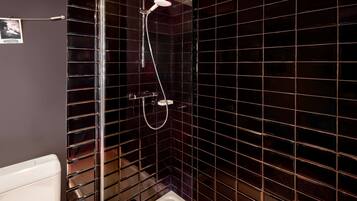 Un baño con paredes de azulejos oscuros, cabina de ducha de vidrio y un inodoro blanco.