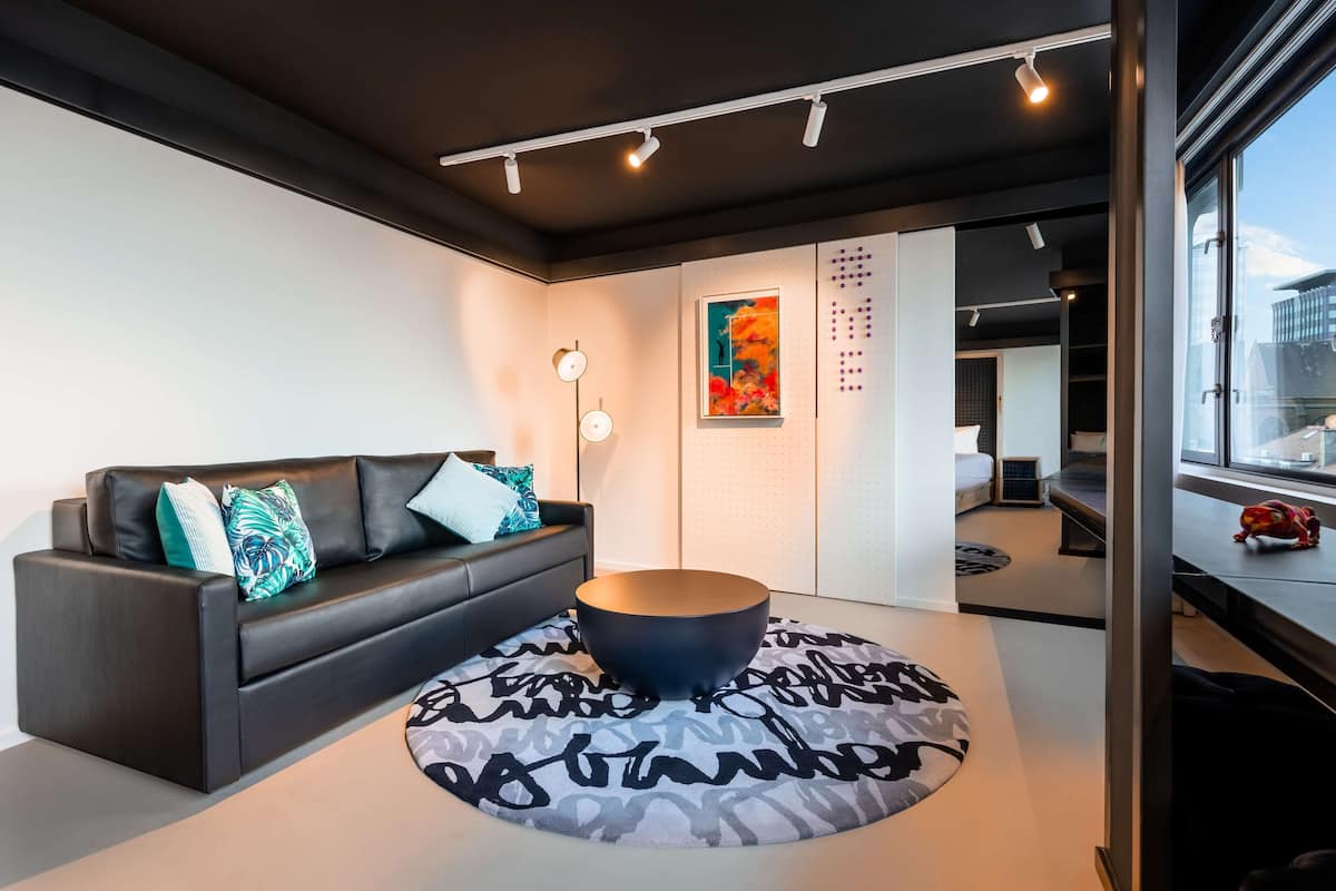 A modern living room with a black leather sofa, a round coffee table, and a patterned rug.