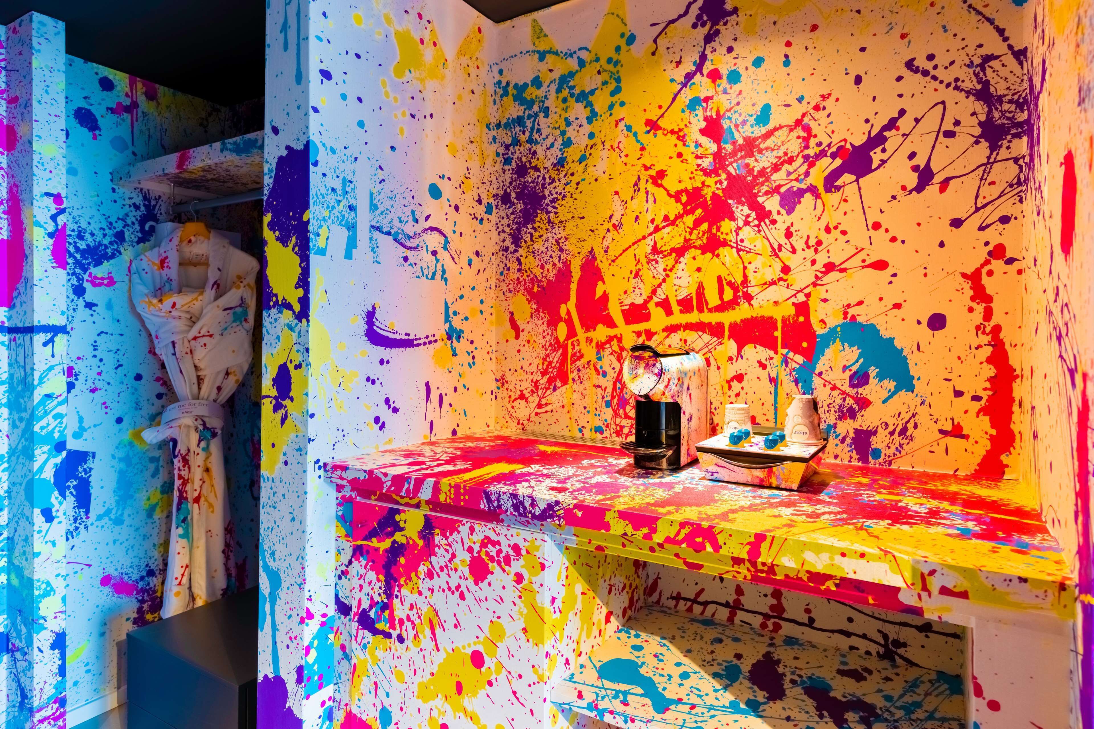 Una habitación con una pared cubierta de salpicaduras de pintura vibrantes y coloridas, y una pequeña mesa con una taza y un platillo.