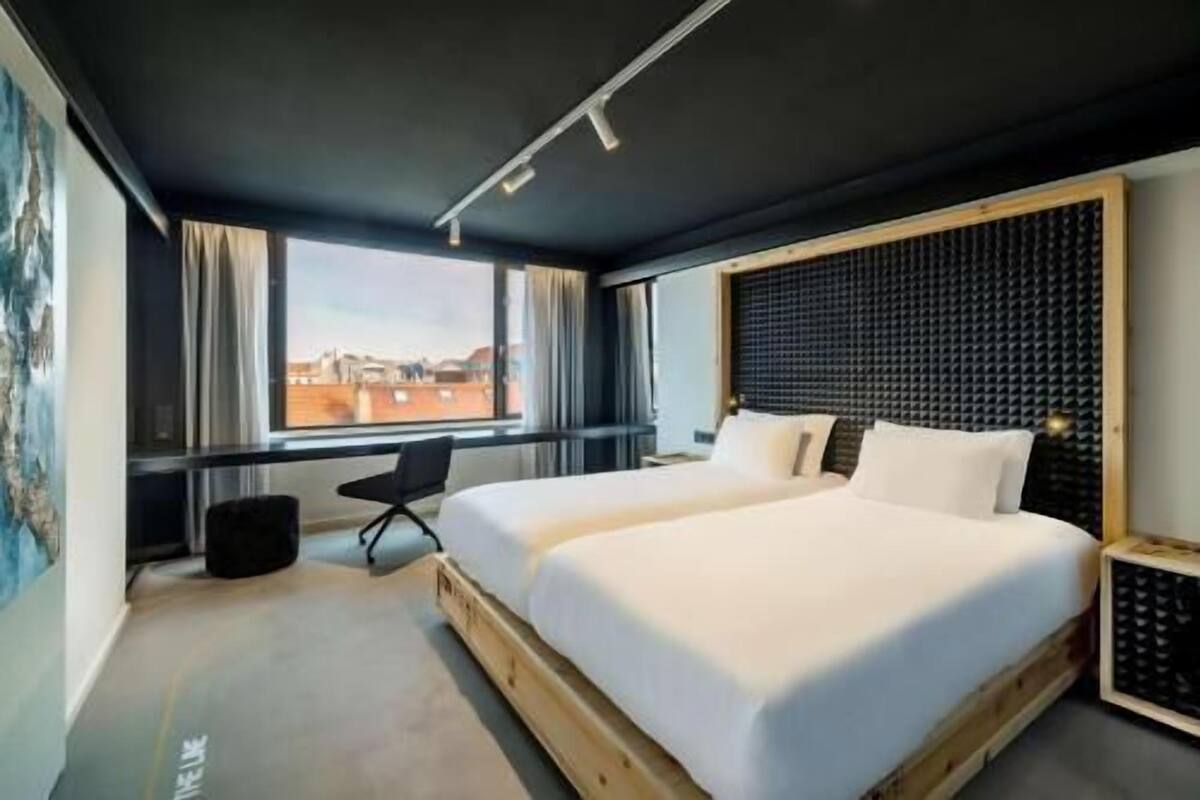 A modern hotel room with two beds, a view of the cityscape, and a large window.