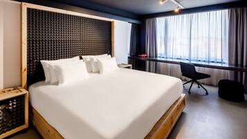 A modern hotel room with a large bed, a wooden headboard, a desk, and a chair.