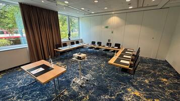 A conference room with a long table, chairs, a projector, and a carpeted floor.