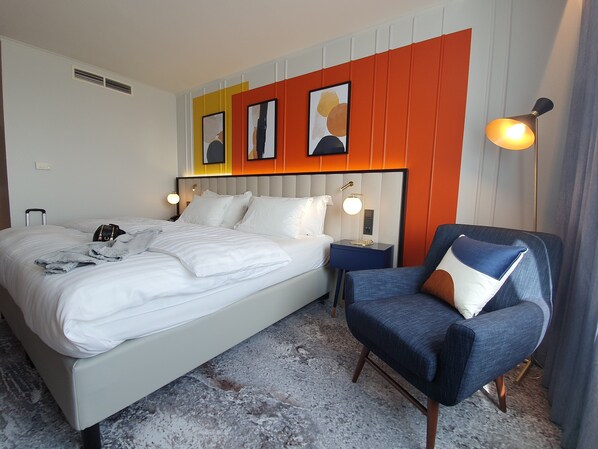 Habitación de hotel con cama, una silla, una mesita de noche y una pared con tres cuadros.