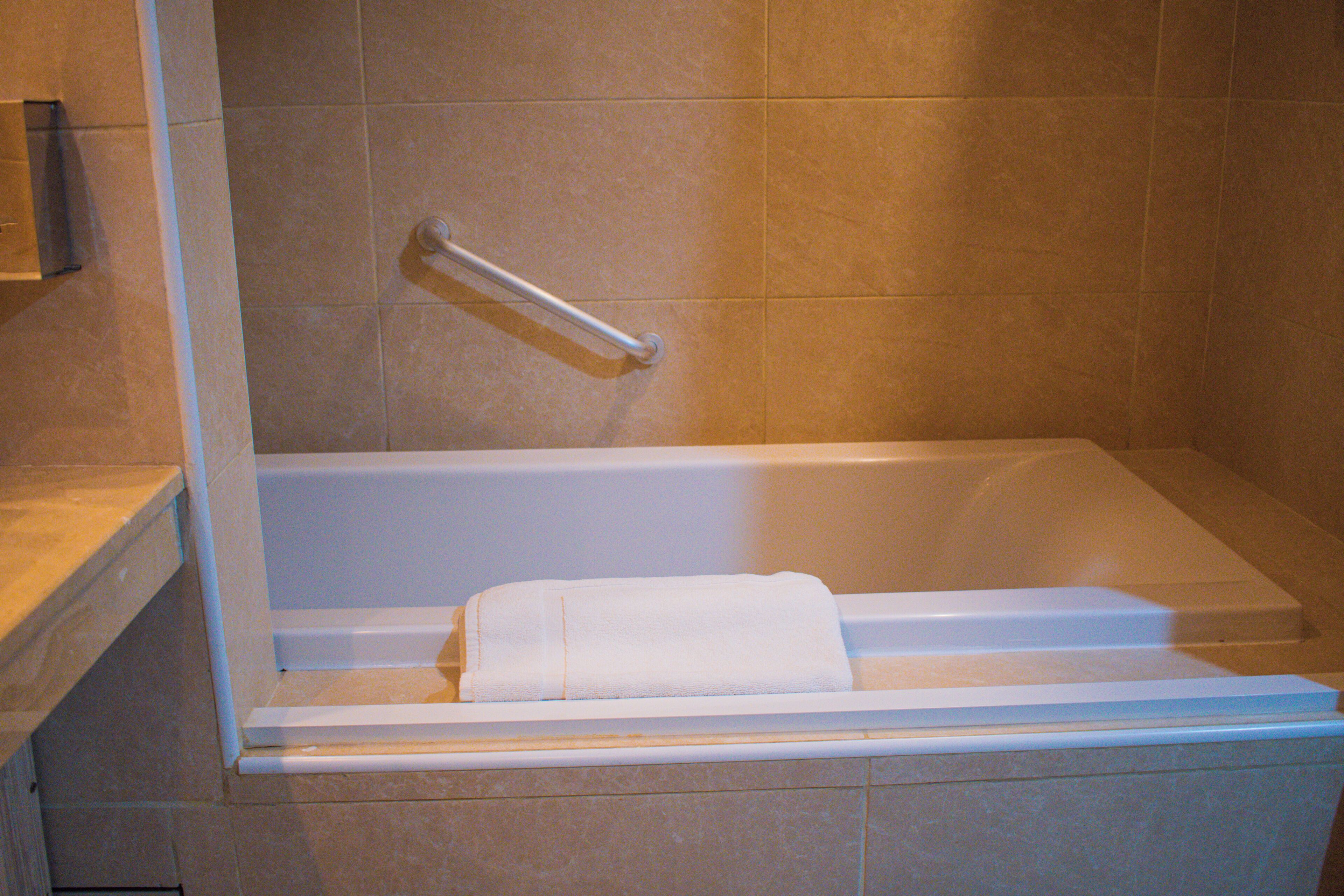 A bathtub with a towel, a grab bar, and a shower curtain rod.