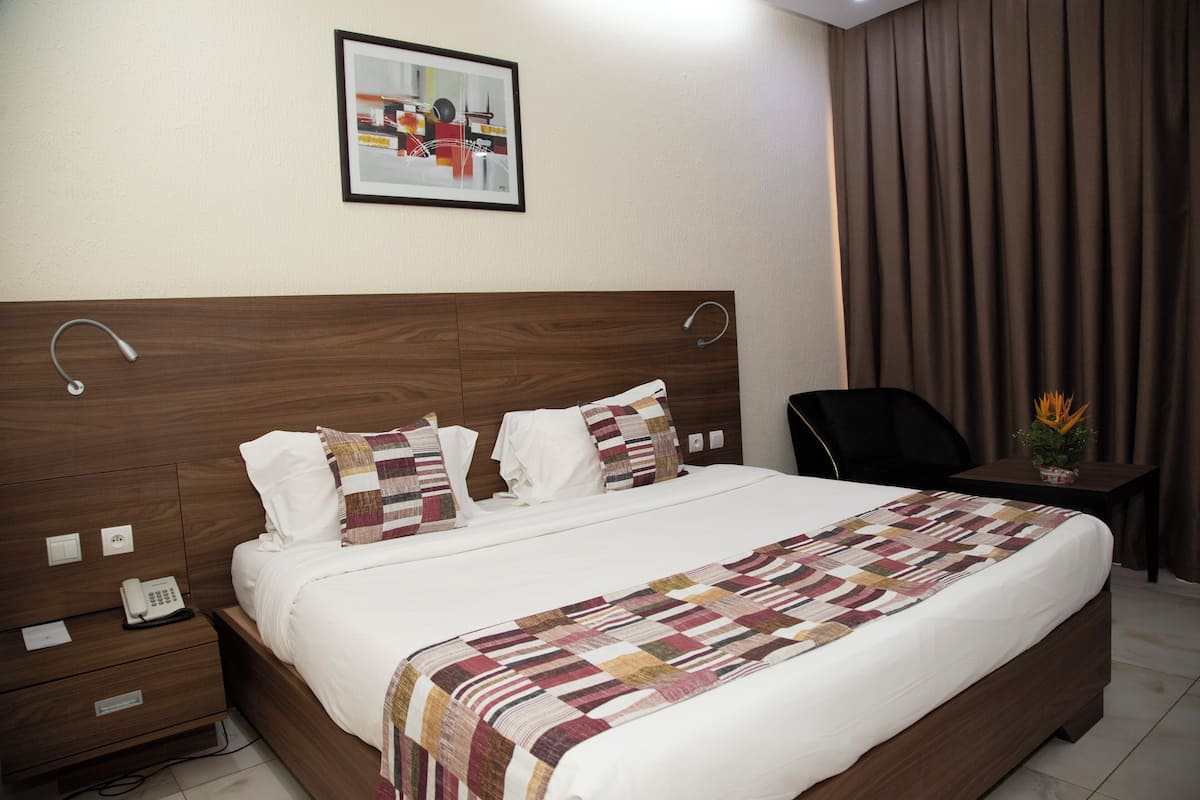 A neatly made bed with a patterned bedspread, a bedside telephone, and a framed picture on the wall.