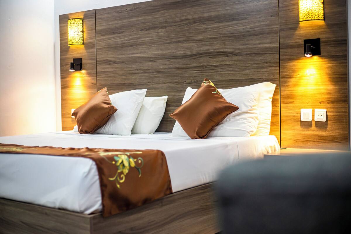 A modern hotel room with a wooden headboard, white bedding, and decorative wall sconces.