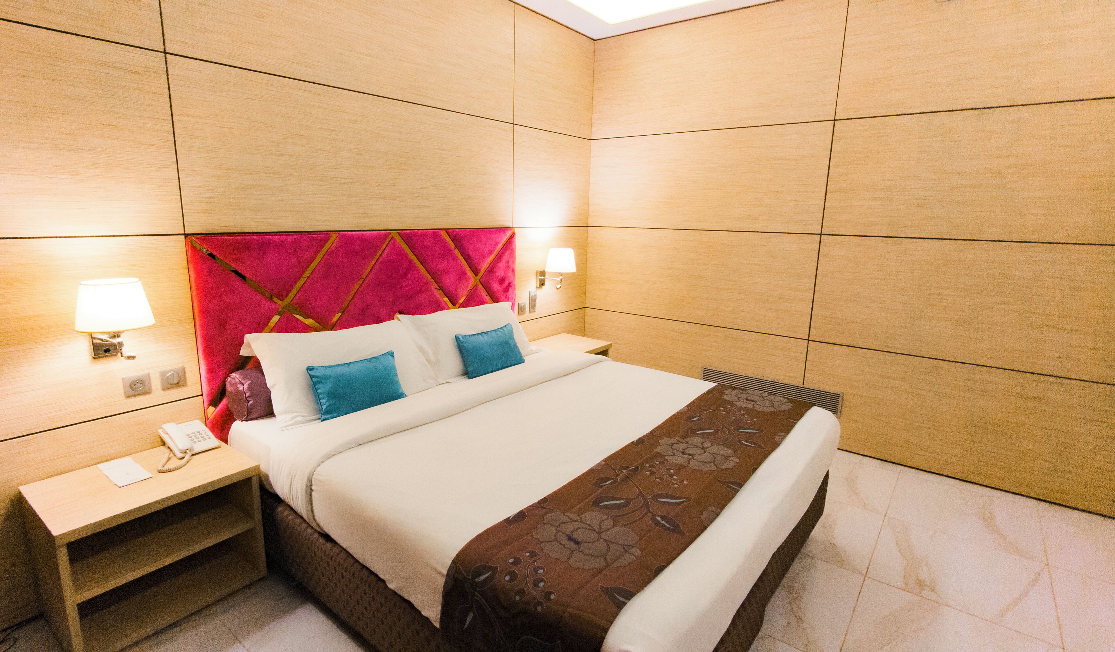 A hotel room with a large bed, two bedside lamps, a nightstand with a phone, and a red accent wall.