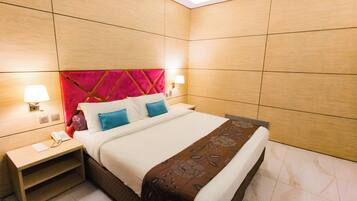 A hotel room with a large bed, two bedside lamps, a nightstand with a phone, and a red accent wall.