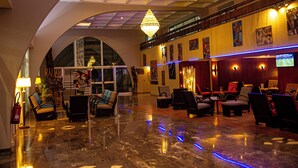 Un hall d’entrée spacieux avec un plafond haut, un sol en marbre et un grand lustre. On y trouve plusieurs coins salon avec des chaises et des tables.