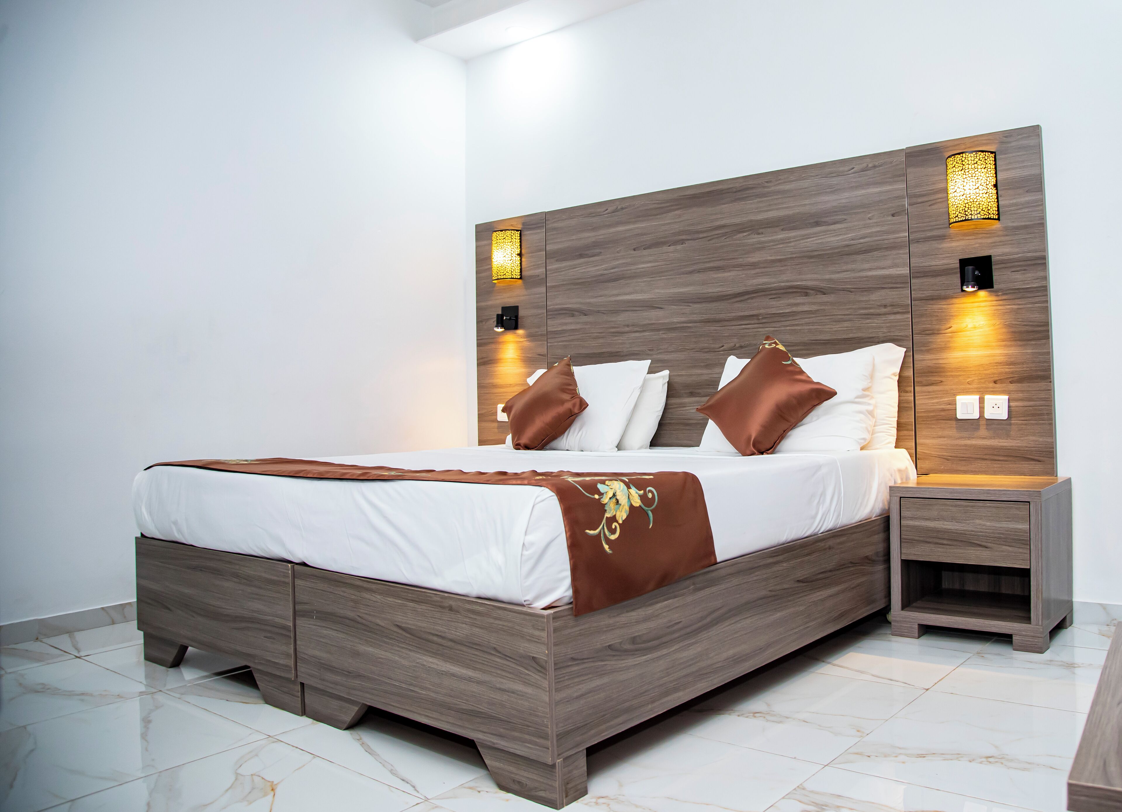 A modern bedroom with a wooden bed, white bedding, and two bedside lamps.