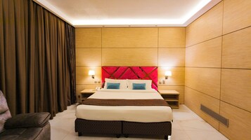 Habitación de hotel con una cama grande, paneles de madera, cabecera roja, dos mesitas de noche con lámparas y una silla.