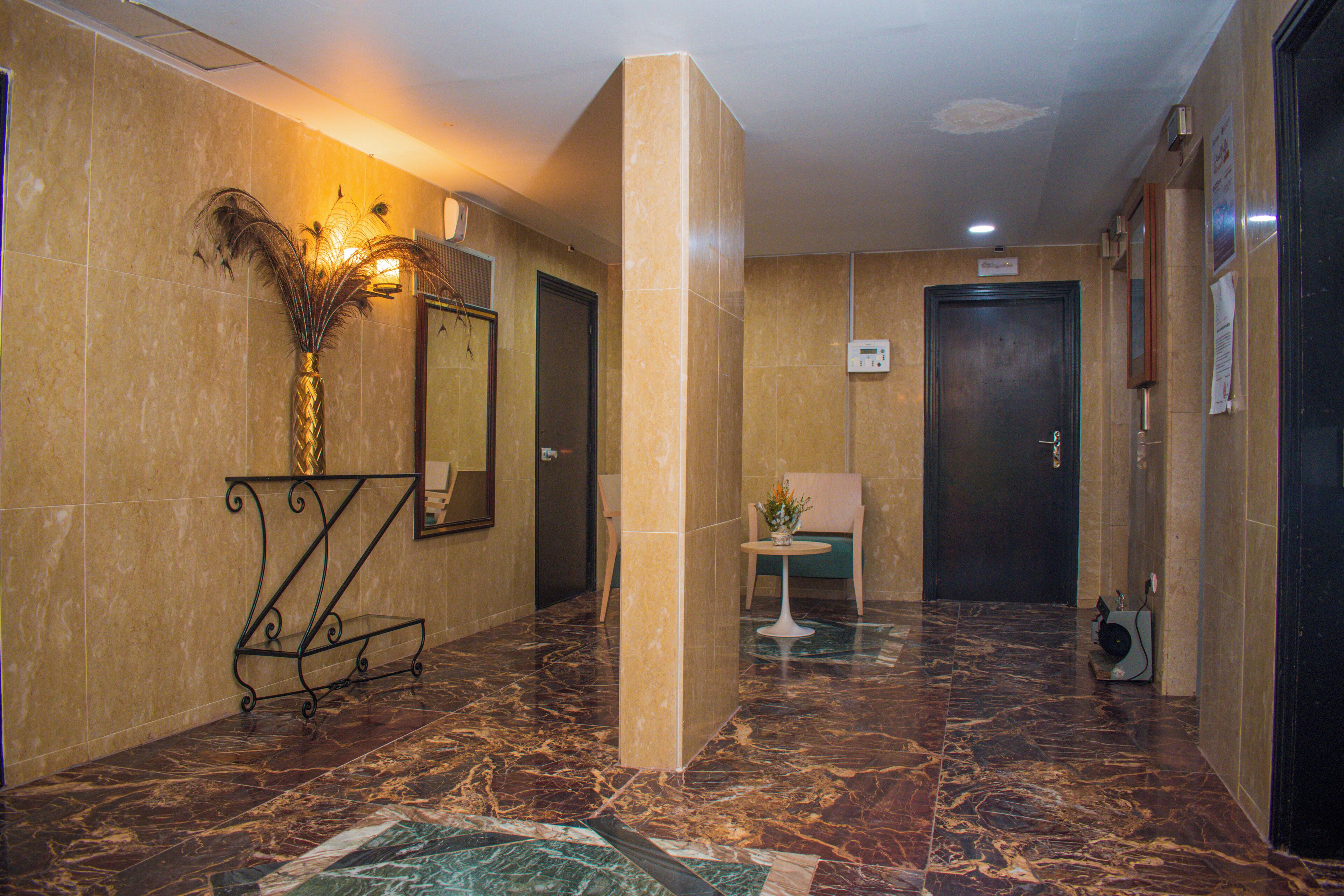 A marble-floored lobby with a reception desk, a vase with dried plants, a wall-mounted mirror, and a door.