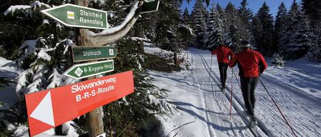 Un cartel con indicaciones para pistas de esquí y un paisaje nevado con esquiadores.